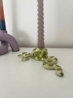 the snake is laying on the table next to the purple and green vase with it's tail curled up