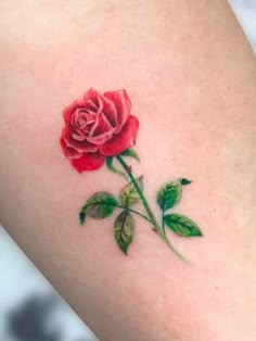 a small rose tattoo on the back of a woman's thigh, with green leaves