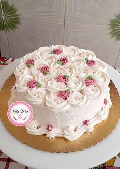 a cake with white frosting and pink roses on top is sitting on a table