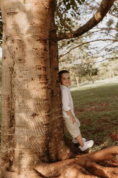 a young boy standing next to a tree