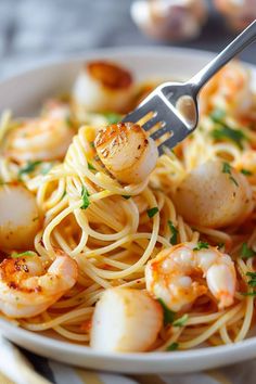 a plate of pasta with shrimp and scallops on the top is being held by a fork