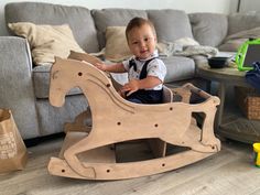 a baby sitting in a wooden rocking horse next to a couch and toys on the floor