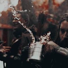 a man with long hair pouring something into a metal cup in front of other people