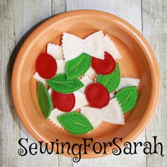 an orange plate topped with red and green felt flowers on top of a wooden table