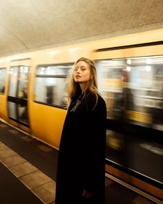 a woman standing in front of a train at a subway station with her head turned to the side