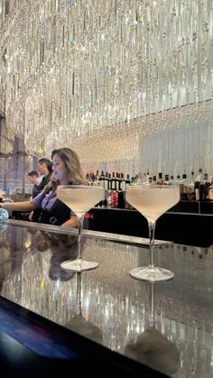 two people sitting at a bar with martinis in front of them and chandelier hanging from the ceiling