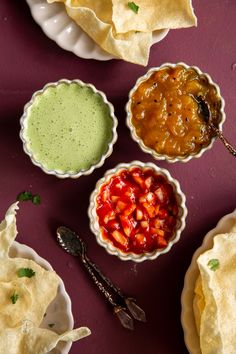 three bowls filled with different kinds of food on top of a purple tablecloth next to chips and salsa