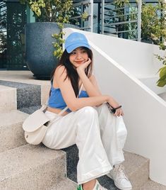 a young woman sitting on the steps with her hand under her chin and wearing a blue hat