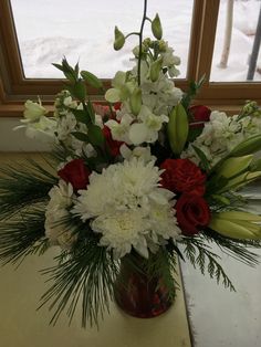 a vase filled with white and red flowers on top of a table next to a window