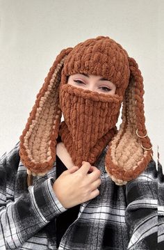 a woman wearing a knitted hat and scarf with ear flaps on her head, covering her face