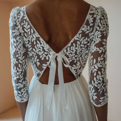 the back of a woman's wedding dress with white lace and bows on it