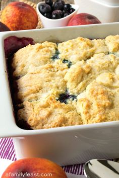 an apple and blueberry cobbler in a white casserole dish with fresh fruit on the side