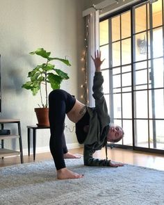 a woman doing a handstand in front of a window with a potted plant