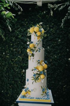 a three tiered cake with lemons and blue flowers on the top is surrounded by greenery