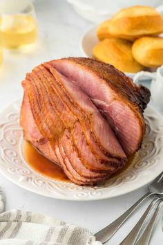 sliced ham on a white plate with silverware next to other food items and utensils