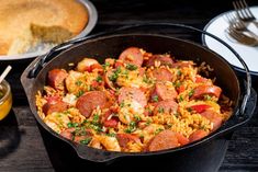 a skillet filled with sausage and rice next to a plate of bread on a table