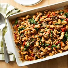 a casserole dish filled with pasta and spinach on a table next to a fork