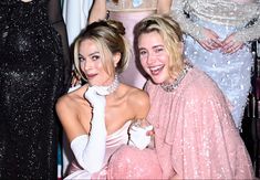 two women sitting next to each other in front of dresses and one is wearing gloves