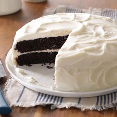 a cake with white frosting is on a plate next to a knife and fork