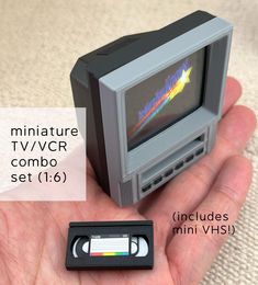 a miniature tv set in the palm of someone's hand next to it is a tape recorder