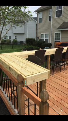 a wooden deck with chairs and tables on it in front of a house next to a fence