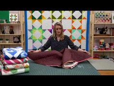 a woman sitting on top of a table next to quilts