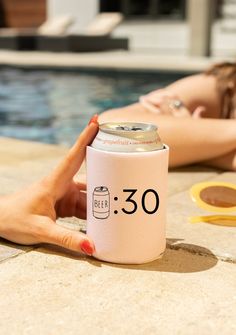 a woman laying next to a swimming pool holding a pink beer can with the number 30 on it