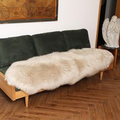 a green couch with white fur on it in front of a wooden floor and wall