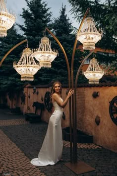 a woman in a white dress is standing under chandeliers and posing for the camera