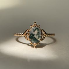 a gold ring with a green and white stone in the center on a white surface