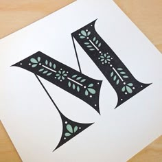 the letter k is made up of black and white paper with green leaves on it