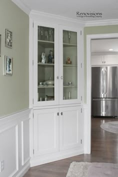 a white china cabinet with glass doors in a living room next to a kitchen area