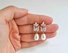 a hand holding a pair of earrings with pearls and leaves on the back of it