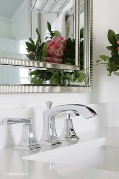 a bathroom sink sitting under a mirror next to a vase with flowers in it on top of a counter