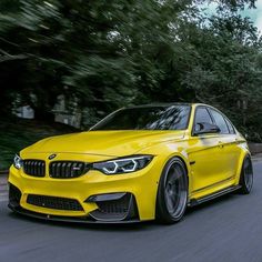 a yellow bmw car driving down the road with trees in the backgrouund