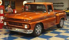 an orange pickup truck parked in a garage next to a gas pump and other antique cars