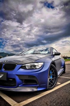 a blue car parked in a parking lot under a cloudy sky with clouds above it