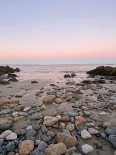 the beach is full of rocks and water at sunset or dawn with pink sky in background