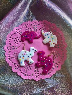 four little dog shaped earrings on a doily with pink and purple lace around them