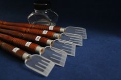 six wooden utensils are lined up next to a glass bottle with labels on them