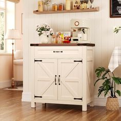 a kitchen area with white cabinets and wooden floors, potted plants on top of the cabinet