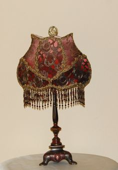 an ornate lamp with red and gold shades on it's base is sitting on a table