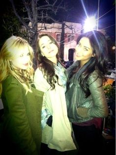 three young women standing next to each other in front of a tree and building at night