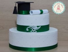 a three tiered white cake with green ribbon and graduation cap on top, sitting on a wooden table