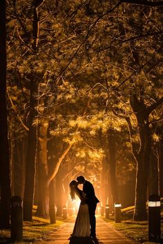 a bride and groom kissing in the middle of a path surrounded by trees at night