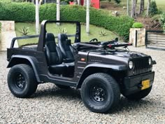 a black jeep is parked on gravel in front of some bushes and trees, with the driver's seat up