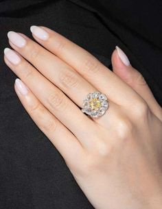 a woman's hand with a yellow diamond ring on her left hand and white nails