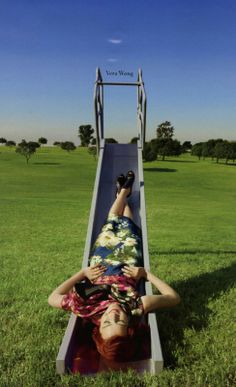 a woman laying on top of a slide in the middle of a grass covered field