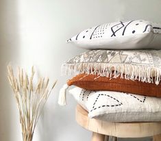 four pillows stacked on top of each other in front of a vase with dried grass