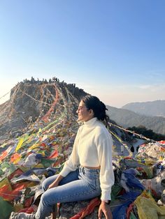 a woman sitting on top of a mountain covered in lots of colorful flags and streamers